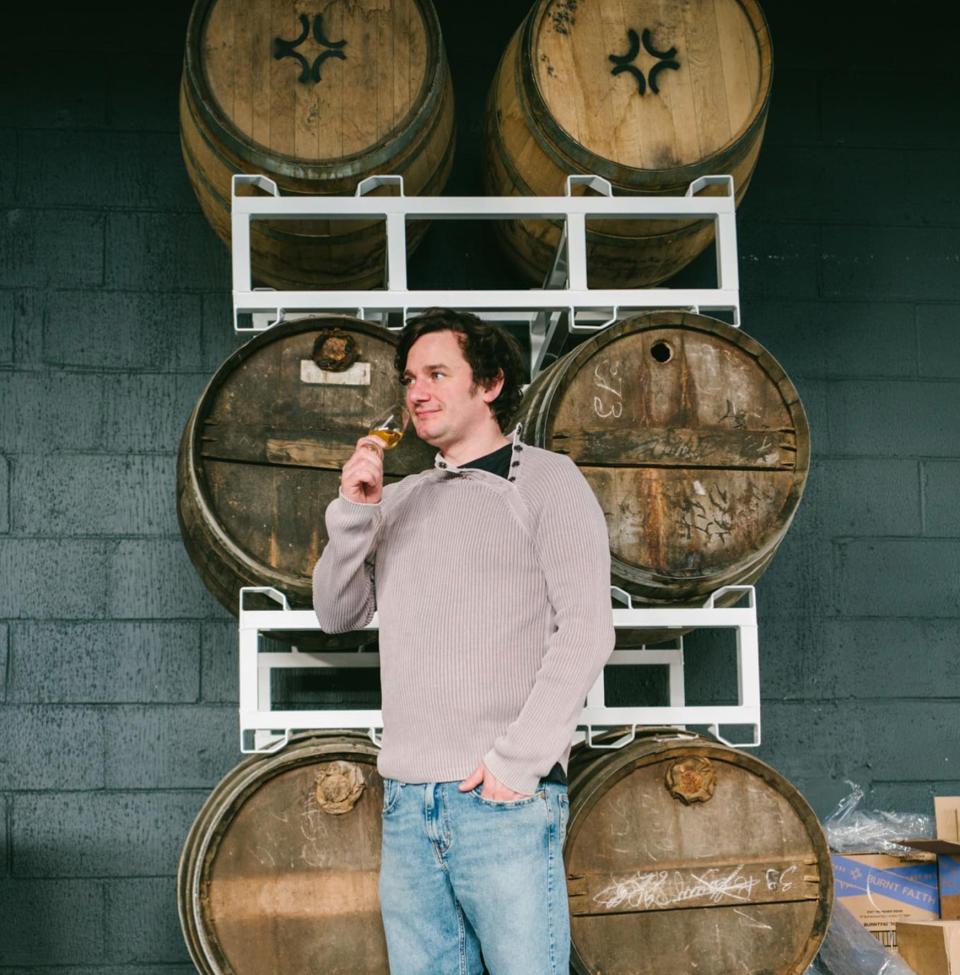 A man standing in front of Burnt Faith casks with a nosing glass